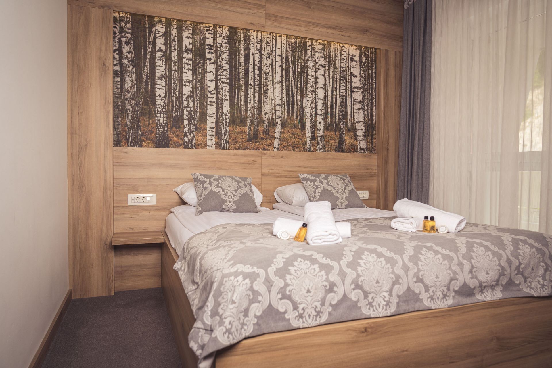 "Double hotel bed with birch forest wall art, wood accents, and elegant bedding in Hotel Tazz in Bihać, Bosnia"